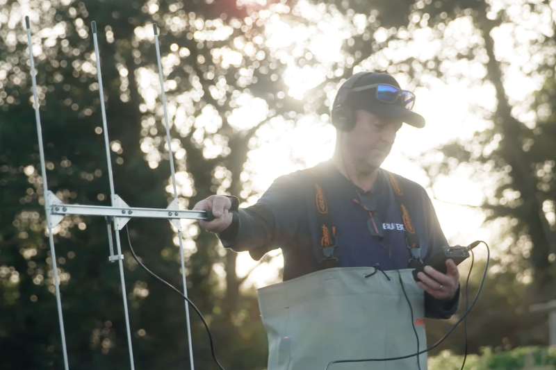 A researcher holds a large aerial in a rural setting 