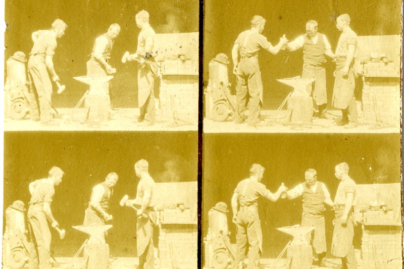 Frames 4 very similar images, in square formation depicting three men in blacksmith's aprons standing by an anvil in the front of what looks like a blacksmith's shop