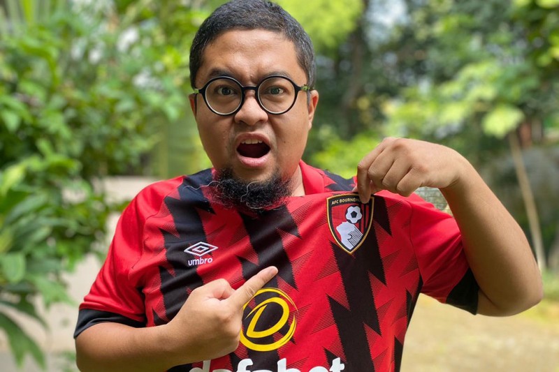 Fuddy Fuddy looking at the camera, wearing an AFCB shirt pointing at the AFCB badge
