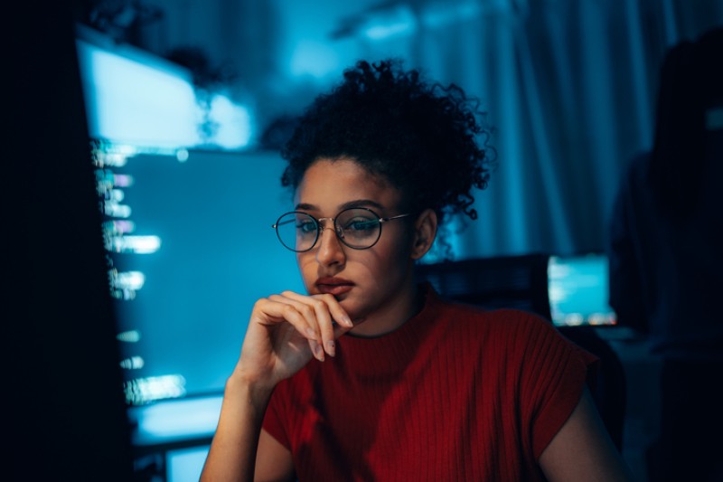A young woman looking at her computer screen with other screens in the background