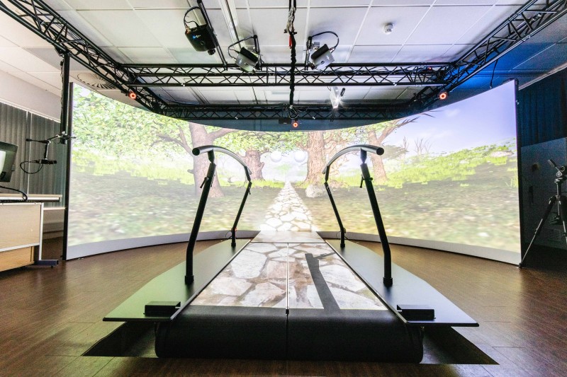 Gait analysis machine A treadmill with computer screens depicting trees and fields in front of it