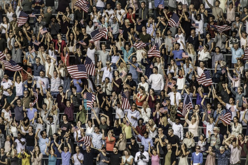 Large crowd of American sports fans on a stadium cheering and waving US flags.