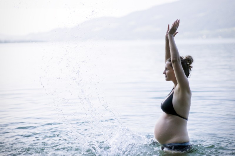A pregnant women standing in a lake with mountains in the background