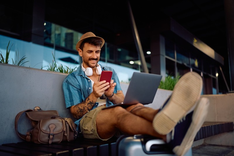 Happy traveler using laptop and smart phone in waiting room at airport terminal.