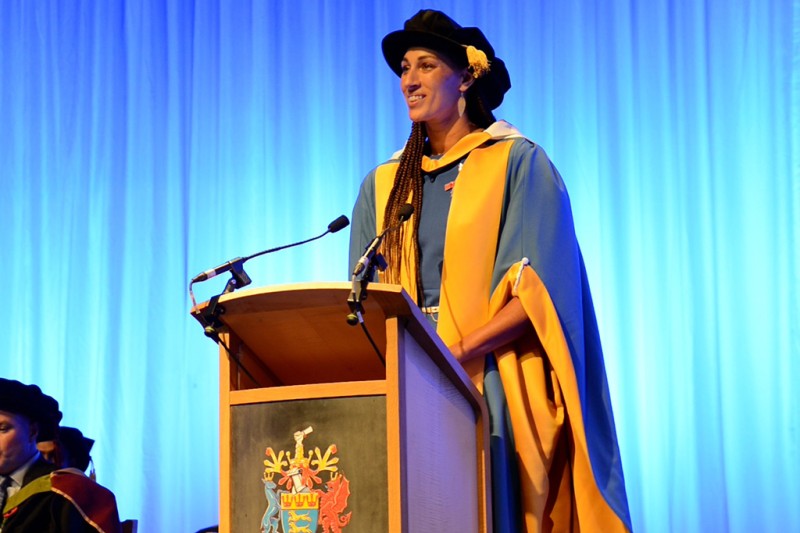 Geva Mentor, standing at a lectern speaking, wearing her ceremonial robes