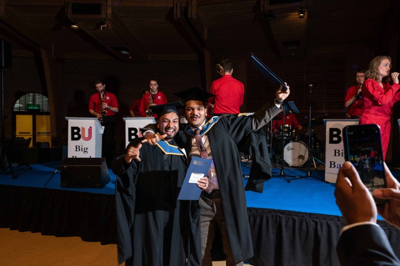 Graduates 2023 Two graduates in their gowns with their arms in the air, standing in front of the band in the reception