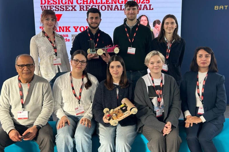Four students standing at the back, three students and two lecturers sitting at the front. All looking at the camera and smiling
