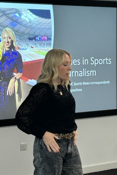 Natalie standing at the front of a lecture theatre with an image of her in a sports stadium projected behind her