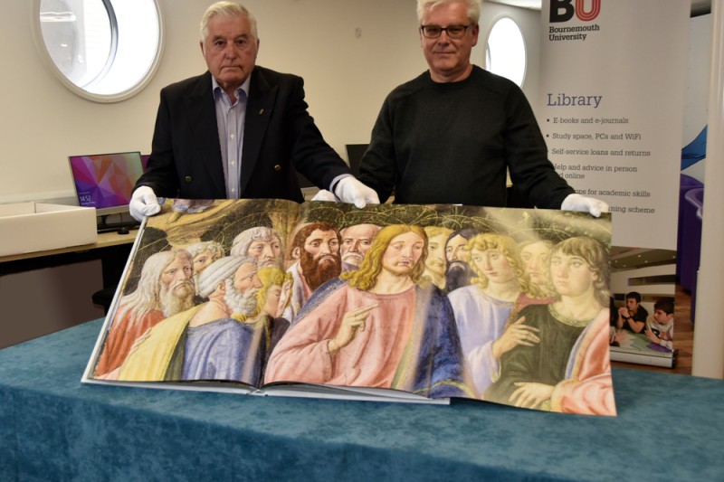 Mr Jack Smith with his son Phillip holding up one of the books open showing a section of a painting