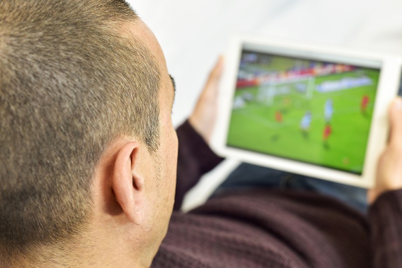 Looking over a man's shoulder as he watches football on his tablet