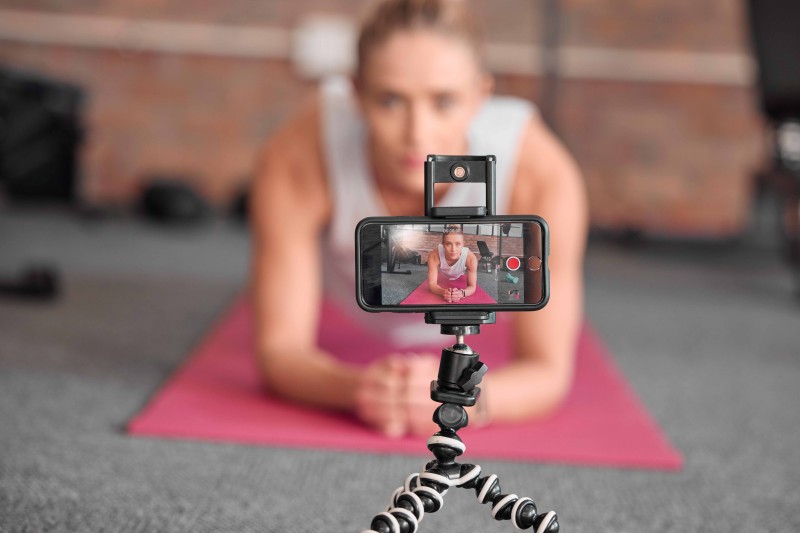 A woman exercising, being filmed by a mobile phone attached to a tripod