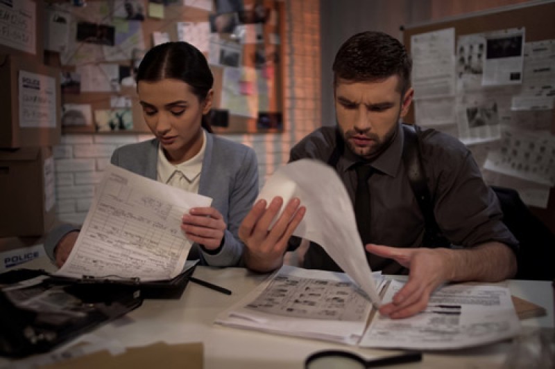 Image A male and a female police officer sitting at a desk working through paperwork, both looking very tired