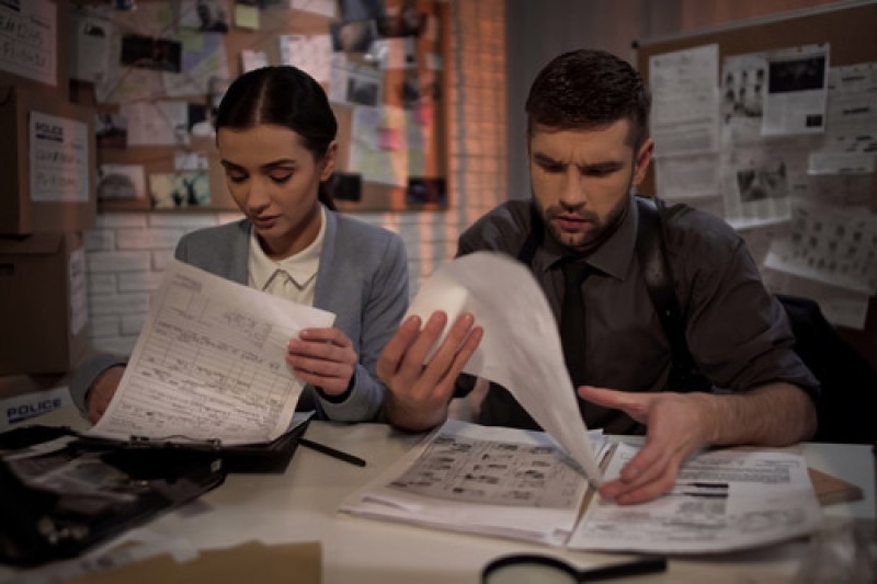 A male and a female police officer sitting at a desk working through paperwork, both looking very tired