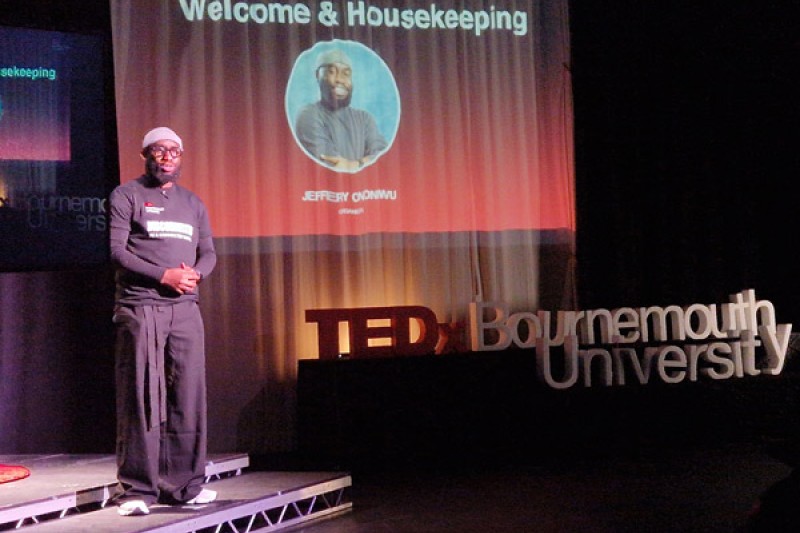 Jeffery Standing on the stage addressing the audience with the TEDx signs around him