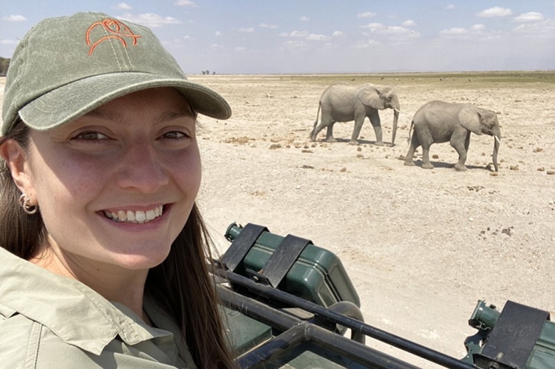 Head and shoulders photo of Katie Thompson smiling at the camera with two elephants in the background