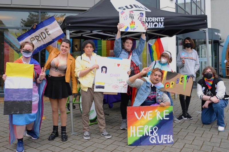A photograph of a group of LGBTQ+ students holding pride banners outside the SUBU building