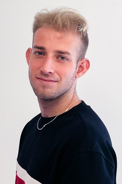 Alumnus Lee is pictured, side on, in front of a white backdrop. He wears a gold chain and a black jumper.