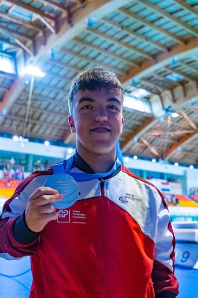 Leo McCrea Leo holding up his medal to the camera at the side of the swimming pool.