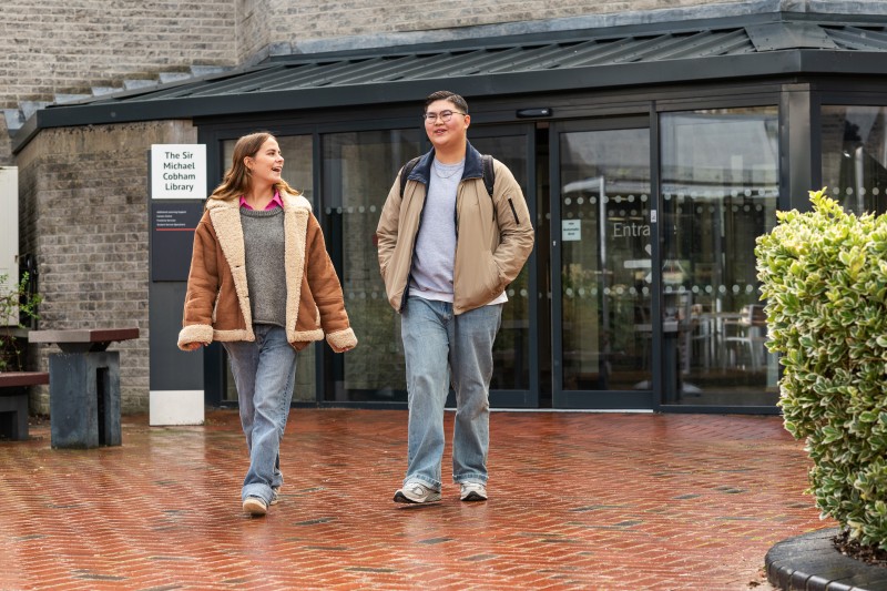 Two students walking out of Sir Michael Cobham Library