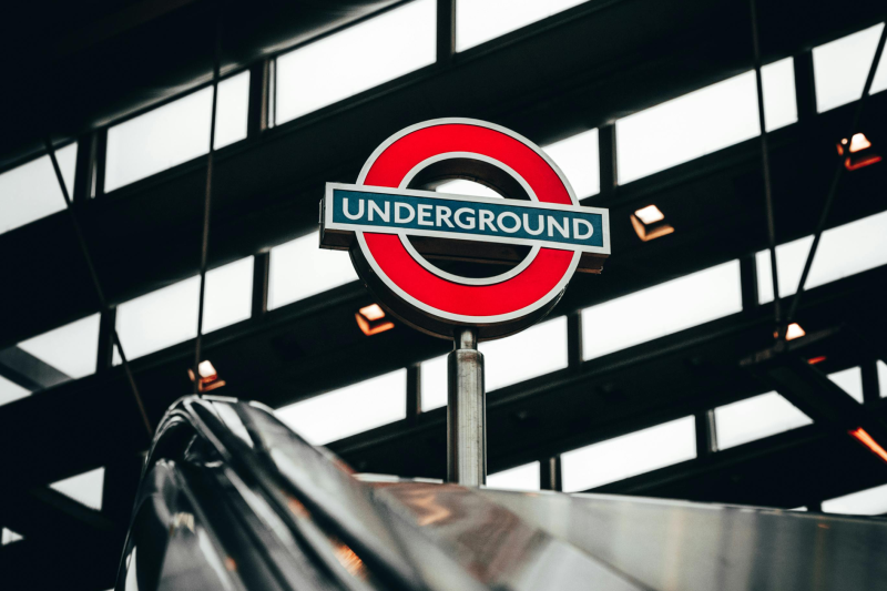 A red and blue London Underground sign at the top of an escalator