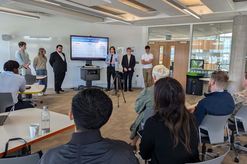 A group of students standing at the front of the room, presenting to a group from the MoD