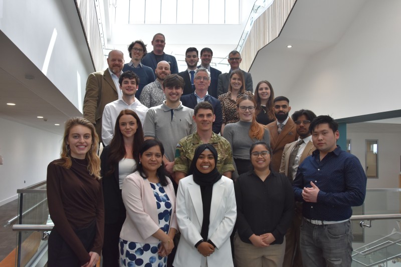 A large group of students and staff from the university and MOD standing on a staircase for a group photo