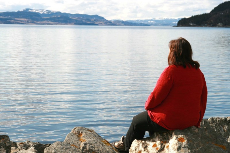 A woman sits on the edge of a lake staring into the water 