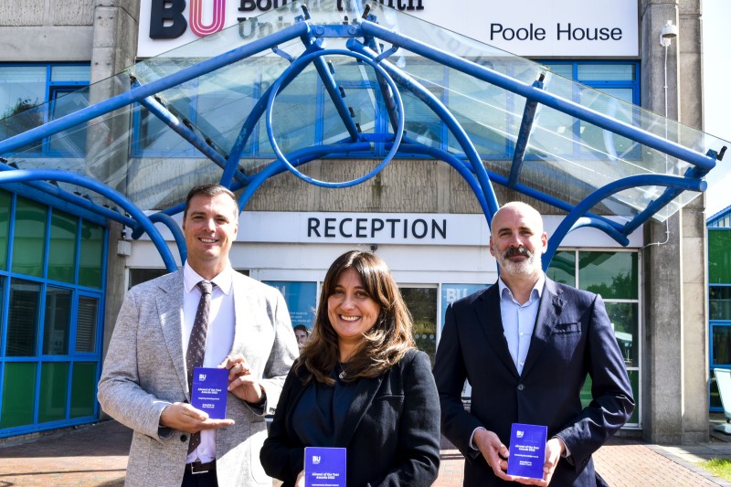 Three award winners holding their awards in front of Poole House, Bournemouth University