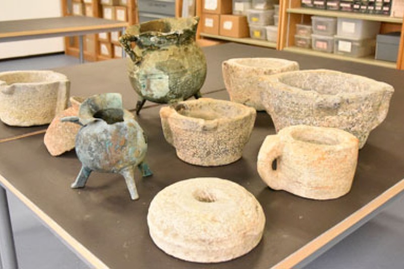 A picture of the contents of the mortar wreck including a couldron, mortar stones, and grinding stones laid out on a table