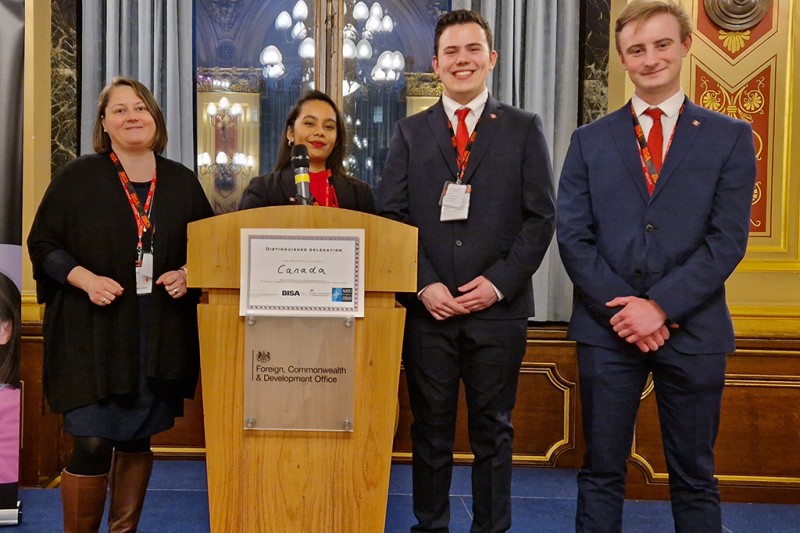 The three students and Alina, at a lectern with the FCDO crest on