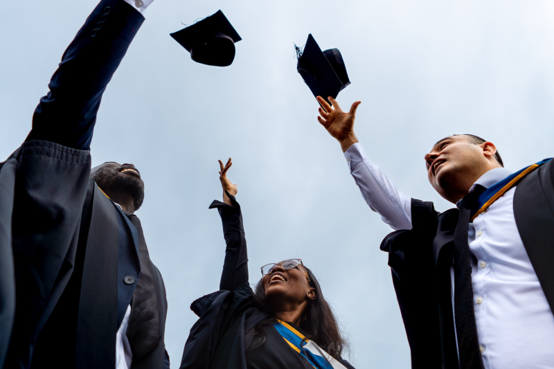 Three graduates throwing their graduation hats