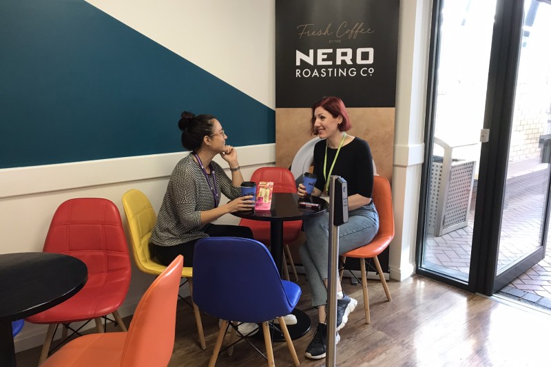 Two students are seated in the library café, talking and laughing