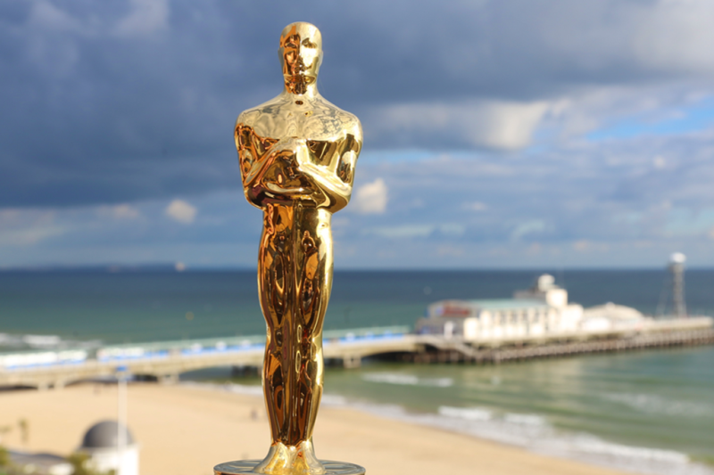 Oscar And Oscar award statue with Bournemouth beach and pier in the background