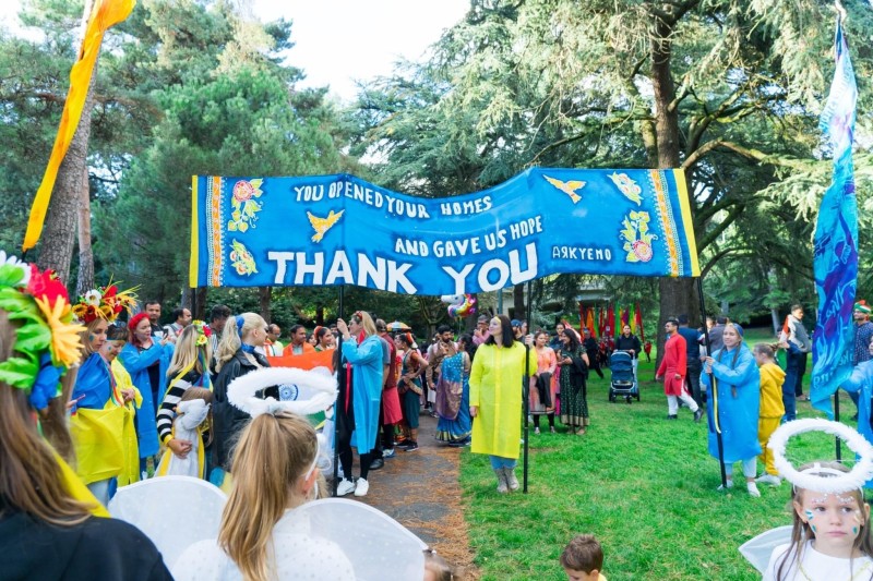 A parade of people wearing the colours of Ukraine's flag with a banner thanking people for taking them in to their homes