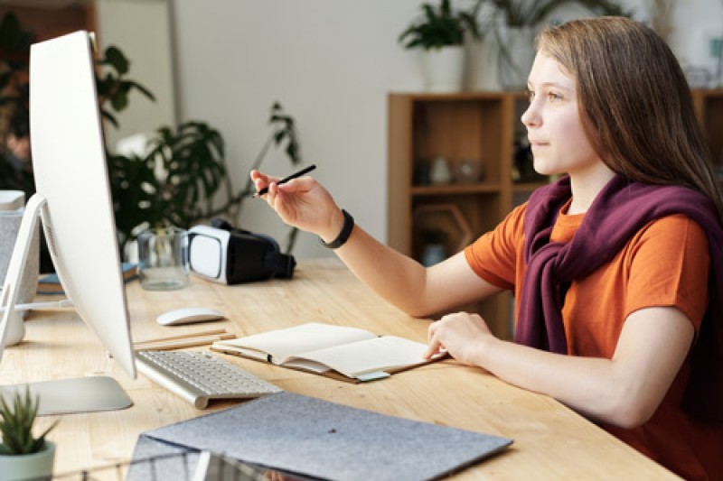 Homework Girl Holding Pencil While Looking at Imac with a notebook in front of here