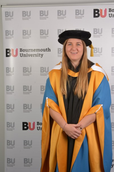 Poppy Cleall in her graduation gown looking at the camera smiling