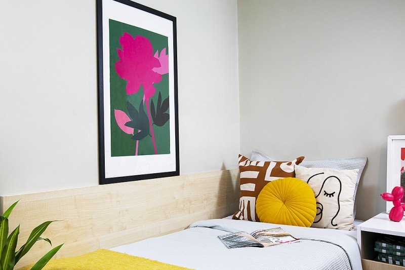 A single bed with a picture of a flower on the wall next to it