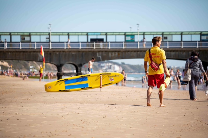 A lifeguard walking on Bournemouth's beach with a pier in the background