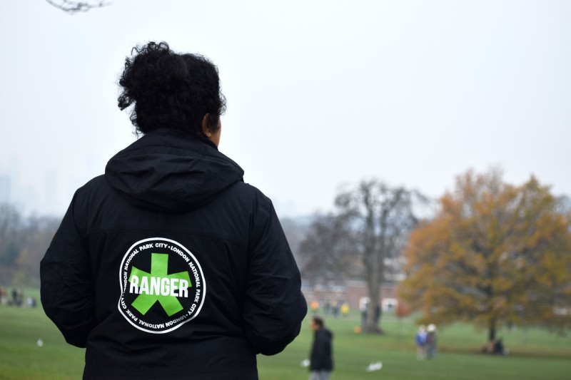 Photo of someone looking out over a park. On the back of their jacket is the words "Ranger - London National Parks City"