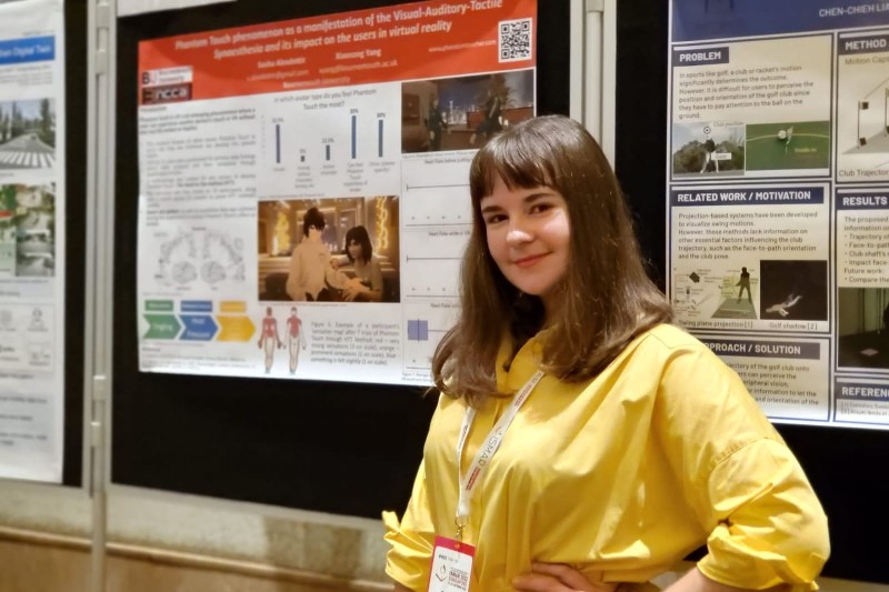 Sasha standing in front of a poster which depicts her work