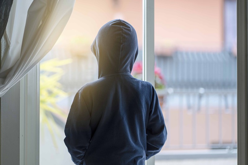 Back of a young boy in a hoody top, looking out a window