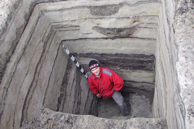 A man standard in a deep Archaeological pit, surrounded by rectangular straight walls