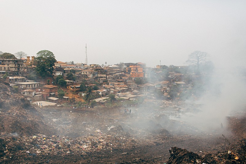 People walking next to Landfill site People walking next to a vast landfill site in Freetown, Sierra Leone, with smoke rising from the site