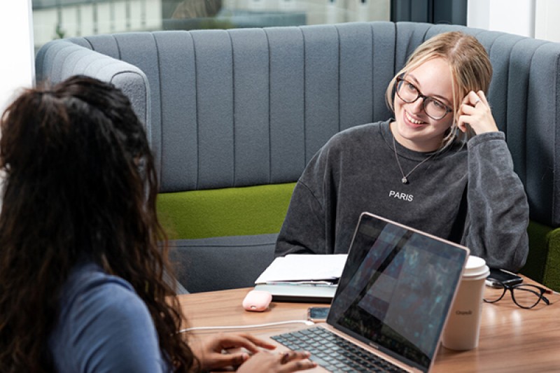 two students in chairs with a laptop