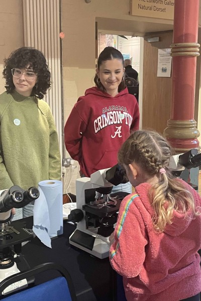 Twi students and a young girl at a table with microscopes on it at an event