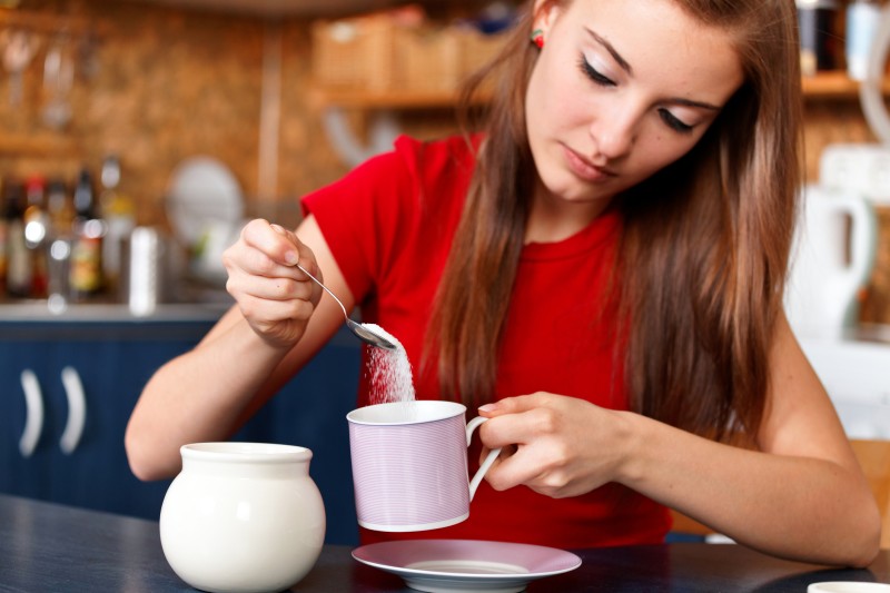 A young woman putting sugar in her drink