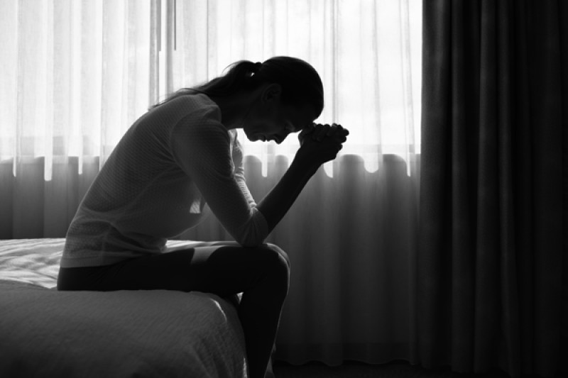 Person sitting on end of bed with head in hands