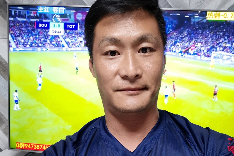 A man stands in front of a TV screen with a football match playing behind him