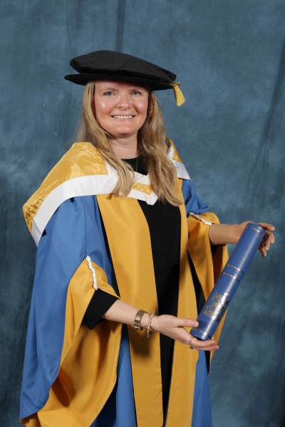 Susie in her ceremonial gowns and hat, holding her certificate. 