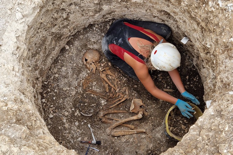 A female archaeologist in a burial pit excavating a skeleton lying in a foetal position